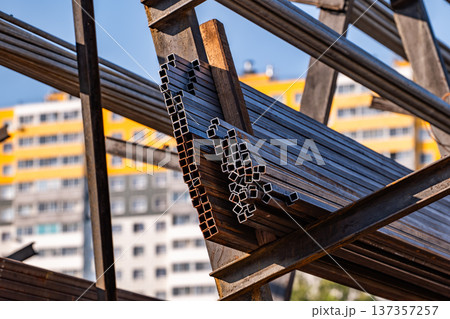 Stacking steel square pipes forming industrial structure against city buildings Stacking steel square pipes forming industrial structure against city buildings 137357257