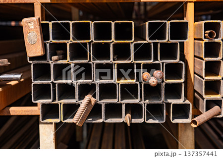 Stacked square steel pipes or metal profiles in a warehouse for industrial construction Stacked square steel pipes or metal profiles in a warehouse for industrial construction 137357441