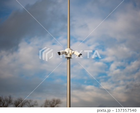 Modern CCTV security cameras on a tall pole against a cloudy blue sky 137357540