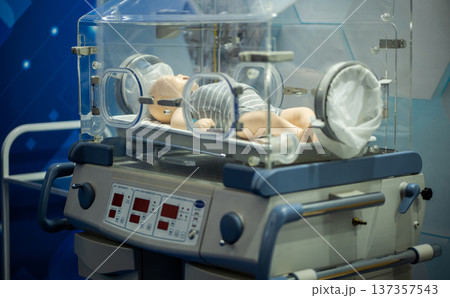 Medical training mannequin of a newborn baby inside a modern infant incubator. 137357543