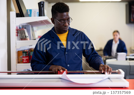 Serious print shop worker cuts paper on professional cutter Serious print shop worker cuts paper on professional cutter 137357569
