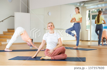 Women doing yoga with group of people in fitness studio, sitting in asana Matsyendrasana Women doing yoga with group of people in fitness studio, sitting in asana Matsyendrasana 137357600