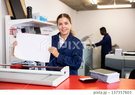 Happy young woman in uniform checking the print quality and accepting color proofs in the printer house Happy young woman in uniform checking the print quality and accepting color proofs in the printer house 137357603