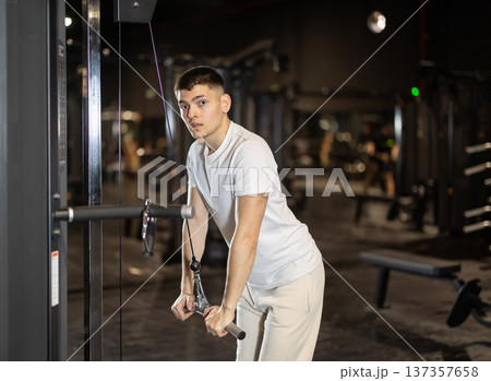 Guy performing triceps pushdowns on cable machine at gym Guy performing triceps pushdowns on cable machine at gym 137357658