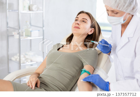Female doctor doing injection to smiling calm young woman in clinic. 137357712