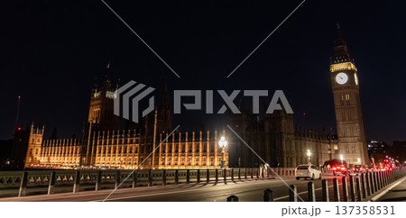 Elizabeth Tower and the Palace of Westminster illuminated at night beside a city road. A red double decker bus travels along the bridge under street lighting. Elizabeth Tower and the Palace of Westminster illuminated at night beside a city road. A red double decker bus travels along the bridge under street lighting. 137358531