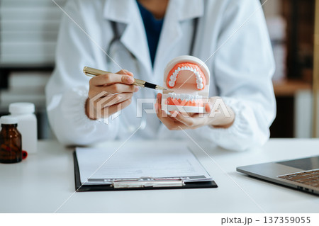 Concentrated dentist sitting at table with jaw samples tooth model and working with tablet and laptop in dental office professional dental clinic. Concentrated dentist sitting at table with jaw samples tooth model and working with tablet and laptop in dental office professional dental clinic. 137359055
