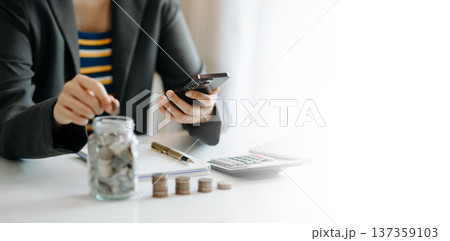 businesswoman holding coins putting in glass with using smartphone and calculator to calculate concept saving money for finance accounting in office 137359103