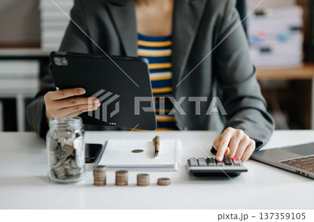 businesswoman holding coins putting in glass with using smartphone and calculator to calculate concept saving money for finance accounting in office 137359105