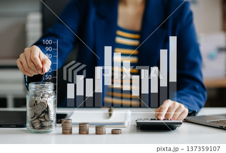 saving money with hand putting coins in jug glass and calculator to calculate budget concept finance and accounting and Gantt chart diagram. screen saving money with hand putting coins in jug glass and calculator to calculate budget concept finance and accounting and Gantt chart diagram. screen 137359107