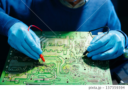Closeup of expert soldering a green PCB board using precision tools. Ideal for electronics, circuit repair, engineering, tech Closeup of expert soldering a green PCB board using precision tools. Ideal for electronics, circuit repair, engineering, tech 137359394