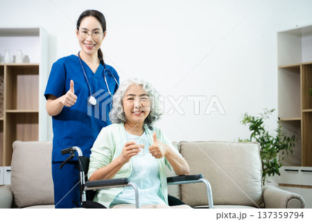 Asian nurse caring for smiling elderly woman in wheelchair at home. Senior care, home healthcare, nursing support, compassion, caregiver service concept Asian nurse caring for smiling elderly woman in wheelchair at home. Senior care, home healthcare, nursing support, compassion, caregiver service concept 137359794