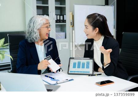 Asian business women discussing finance data using tablet and calculator in a modern office, showing teamwork, mentorship, analysis, and professional corporate collaboration. Asian business women discussing finance data using tablet and calculator in a modern office, showing teamwork, mentorship, analysis, and professional corporate collaboration. 137359899