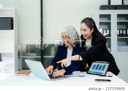 Asian business women discussing finance data using tablet and calculator in a modern office, showing teamwork, mentorship, analysis, and professional corporate collaboration. 137359900