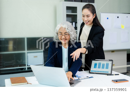 Businesswomen work and discuss their business plans. A Human employee explains and shows her colleague the results paper in modern office. 137359901