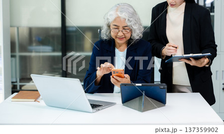 Businesswomen work and discuss their business plans. A Human employee explains and shows her colleague the results paper in modern office. 137359902