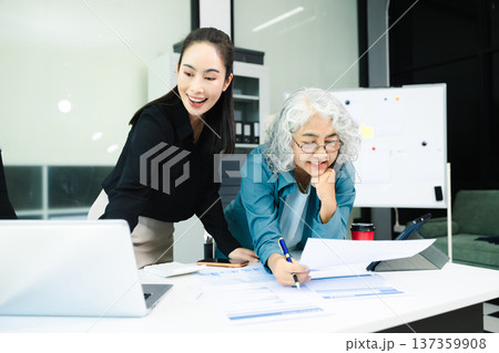 Senior and junior Asian businesswomen discussing documents in modern office, mentorship, teamwork, leadership 137359908