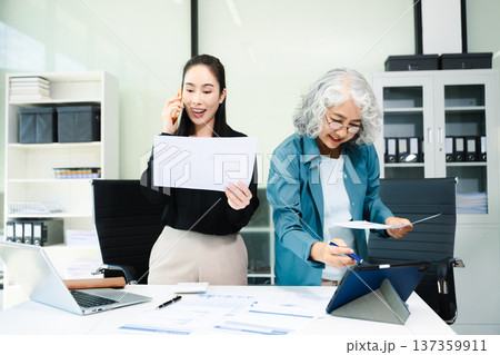 Senior and junior Asian businesswomen discussing documents in modern office, mentorship, teamwork, leadership Senior and junior Asian businesswomen discussing documents in modern office, mentorship, teamwork, leadership 137359911