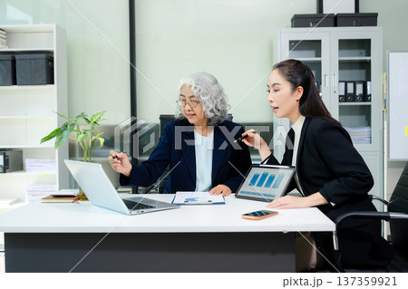 The scene highlights asian business professionals reviewing data and reports together, showing teamwork, mentorship, and strategic planning 137359921