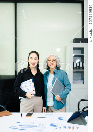 Confident Asian businesswomen standing in modern office. Leadership, teamwork, mentoring and corporate success concept with laptop and documents. Confident Asian businesswomen standing in modern office. Leadership, teamwork, mentoring and corporate success concept with laptop and documents. 137359934