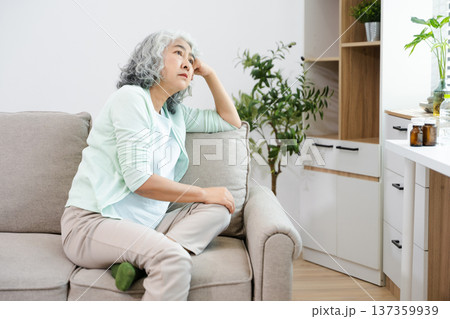 Depressed senior woman holding medication at home. Elderly mental health, loneliness, anxiety, sadness and healthcare concept in living room. 137359939