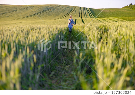 A mother and her young daughter walk hand-in-hand through a lush green wheat field during golden hour A mother and her young daughter walk hand-in-hand through a lush green wheat field during golden hour 137363024