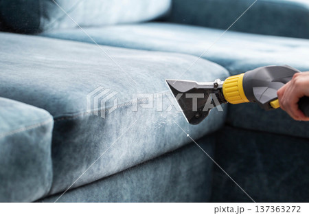 Process of professional deep cleaning upholstery fabric of a sofa with a wet vacuum cleaner, spraying water and detergent on textile surface for thorough sanitation 137363272