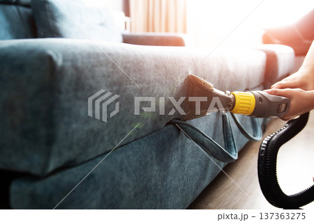 Close-up view of hands operating professional wet vacuum cleaner attachment during deep cleaning of fabric sofa upholstery, ensuring hygiene and freshness 137363275