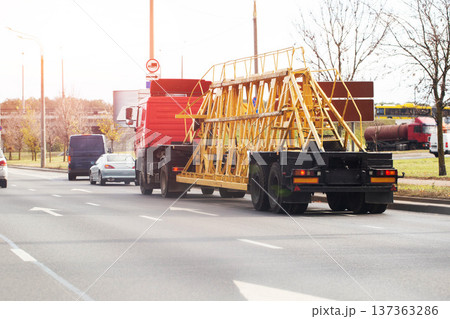 Red heavy semi-truck transports large metal construction structure on highway during daylight traffic. Oversized cargo delivery on multi-lane road. Red heavy semi-truck transports large metal construction structure on highway during daylight traffic. Oversized cargo delivery on multi-lane road. 137363286