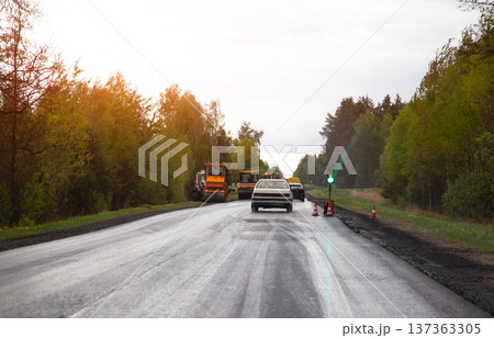Automobiles wait at temporary traffic signal during ongoing road construction project on rural highway with bright sun flare effect. Copy space for text Automobiles wait at temporary traffic signal during ongoing road construction project on rural highway with bright sun flare effect. Copy space for text 137363305