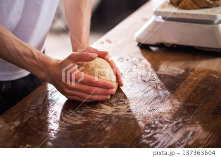 Detailed view of hands of artisan baker vigorously kneading dough on flour-dusted wooden countertop, essential step in making fresh, homemade bread product Detailed view of hands of artisan baker vigorously kneading dough on flour-dusted wooden countertop, essential step in making fresh, homemade bread product 137363604