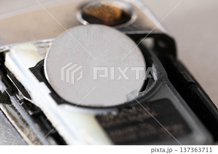 Button cell battery inside open car key remote, close-up view of electronic device power component for maintenance and replacement service. Button cell battery inside open car key remote, close-up view of electronic device power component for maintenance and replacement service. 137363711