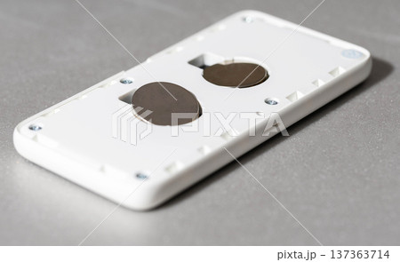White electronic device with back cover removed revealing two button cell batteries for replacement or maintenance. Modern technology gadget on grey surface for service White electronic device with back cover removed revealing two button cell batteries for replacement or maintenance. Modern technology gadget on grey surface for service 137363714