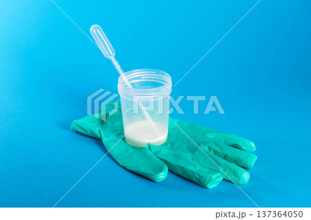 A container with prostate fluid and ejaculate stands on a medical glove against a blue background. Conceptual study of protozoan infection and decreased hormones and libido. Prostatitis and A container with prostate fluid and ejaculate stands on a medical glove against a blue background. Conceptual study of protozoan infection and decreased hormones and libido. Prostatitis and 137364050