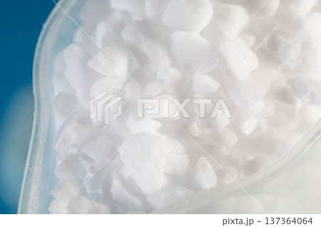 Macro detail view of white crystal granules inside clear plastic container against blurred blue background for cleaning product concept 137364064