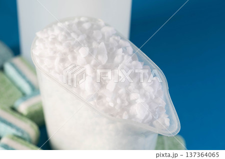 White granular dishwasher salt in clear measuring cup, with bottle of rinse aid and stacked cleaning tablets, essential for efficient dishwashing machine operation 137364065