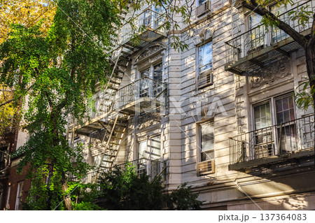 Classic New York residential building facade with fire escape and leafy trees Classic New York residential building facade with fire escape and leafy trees 137364083