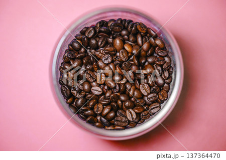 Roasted coffee beans in a glass jar on a pink background top view. Minimalist composition of dark coffee beans in container over pink surface. 137364470