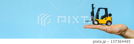Forklift truck balanced on a human hand isolated on a white background. Concept showcasing logistics management Forklift truck balanced on a human hand isolated on a white background. Concept showcasing logistics management 137364485