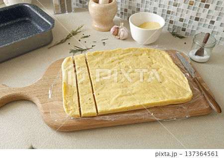 Anonymous person cut hard polenta into pieces with knife on table. Corn flour in the kitchen. Ingredients and traditional Italian cuisine. Anonymous person cut hard polenta into pieces with knife on table. Corn flour in the kitchen. Ingredients and traditional Italian cuisine. 137364561
