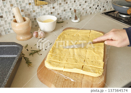 Anonymous person cut hard polenta into pieces with knife on table. Corn flour in the kitchen. Ingredients and traditional Italian cuisine. 137364574