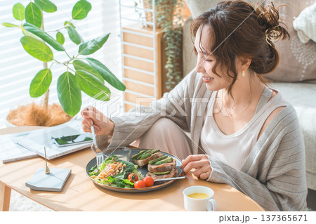 リビングテーブルで食事をするおしゃれな若いアジア人女性 リビングテーブルで食事をするおしゃれな若いアジア人女性 137365671