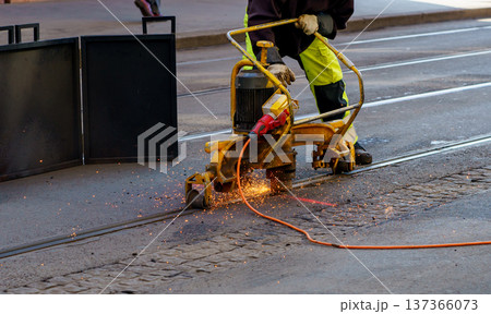 Close up of construction worker grinding tram rails with heavy machine. Urban maintenance, infrastructure repair, roadworks and industry concept. Close up of construction worker grinding tram rails with heavy machine. Urban maintenance, infrastructure repair, roadworks and industry concept. 137366073