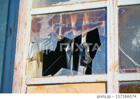 Damaged window with torn plastic sheet and taped cracks. Urban decay, abandonment, renovation need and architectural deterioration concept 137366074
