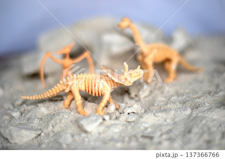 Three toy dinosaur skeletons stand on a table against the backdrop of an excavation site. Three toy dinosaur skeletons stand on a table against the backdrop of an excavation site. 137366766