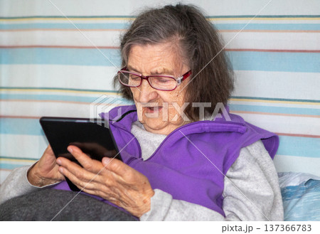 Elderly woman using tablet at home, relaxed senior reading and enjoying digital technology Elderly woman using tablet at home, relaxed senior reading and enjoying digital technology 137366783