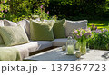 Modern garden sofa with cozy cushions and a coffee table adorned with a fresh flower bouquet in a sunny backyard setting 137367723