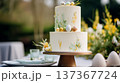 Celebrating Easter with a decorated two tier cake featuring frosting paint and candy eggs on an outdoor table setting 137367724
