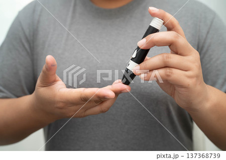 Asian woman self testing to check blood sugar level diabetes by digital lancet on finger at home. Asian woman self testing to check blood sugar level diabetes by digital lancet on finger at home. 137368739