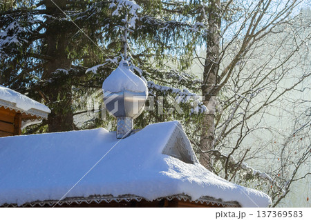 Snow-covered cabin roof adorned with a decorative metal finial surrounded by snowy trees in a tranquil winter landscape Snow-covered cabin roof adorned with a decorative metal finial surrounded by snowy trees in a tranquil winter landscape 137369583